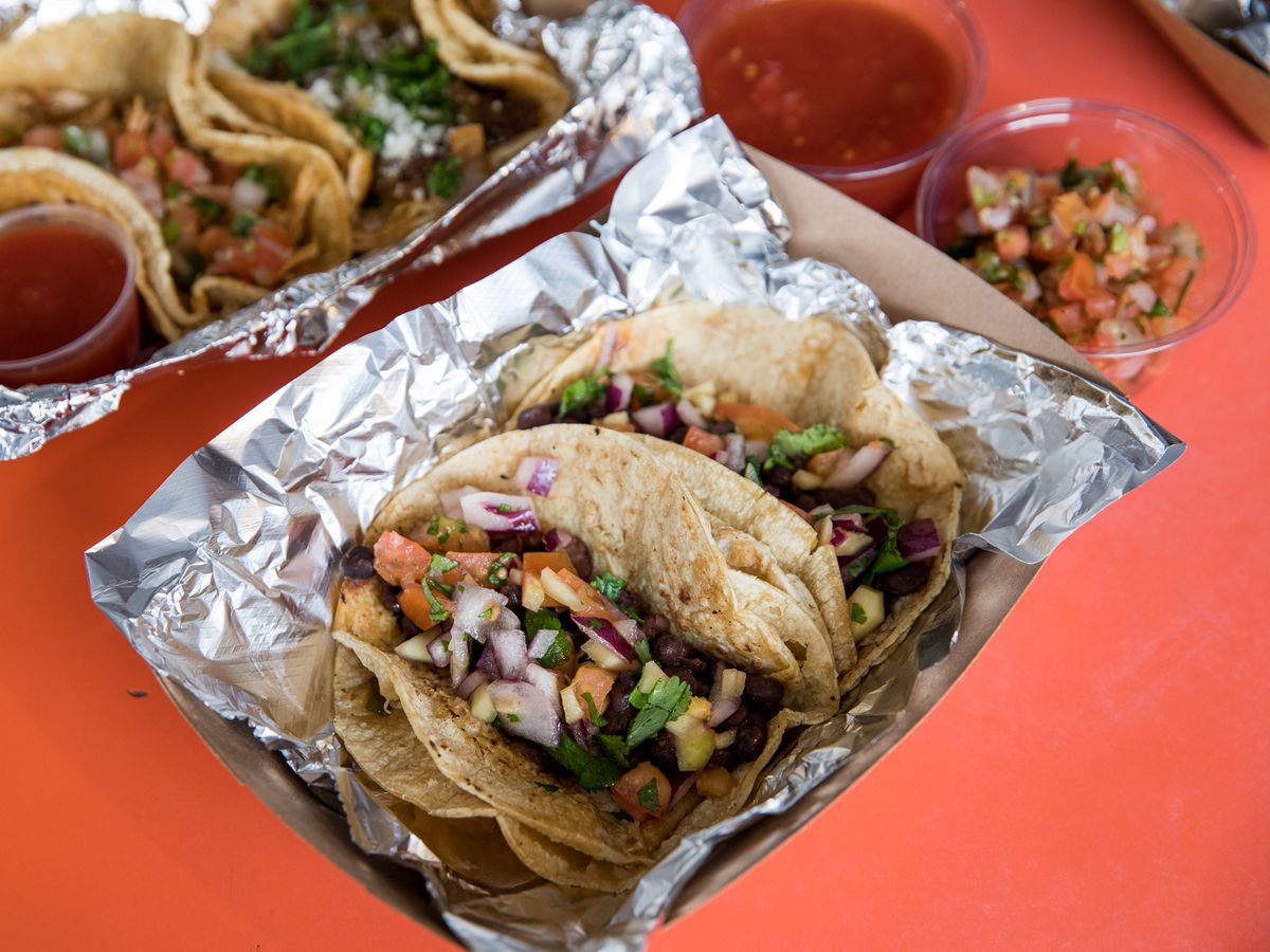 Two tacos surrounded by tin foil in a boat on a red background.