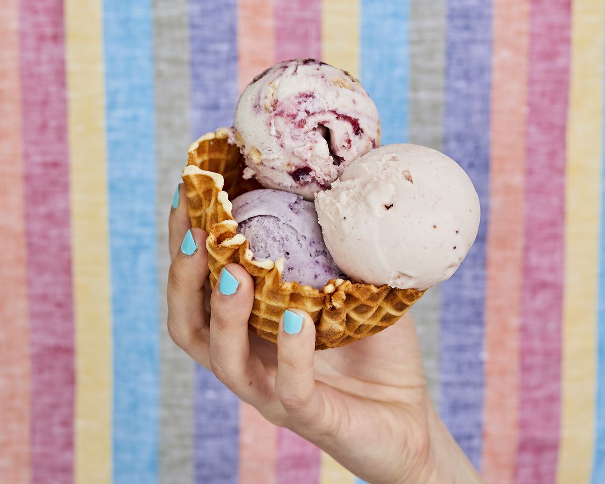 A hand holding a waffle cone bowl filled with three scoops of ice cream.