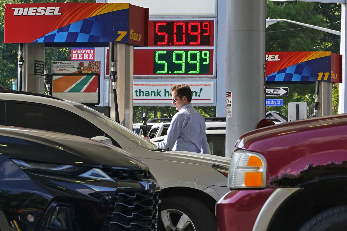 A gas station crowded with cars displays prices per gallon over $5.