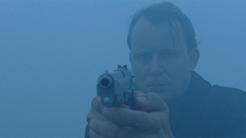A medium-shot of a man holding a pistol surrounded by fog.
