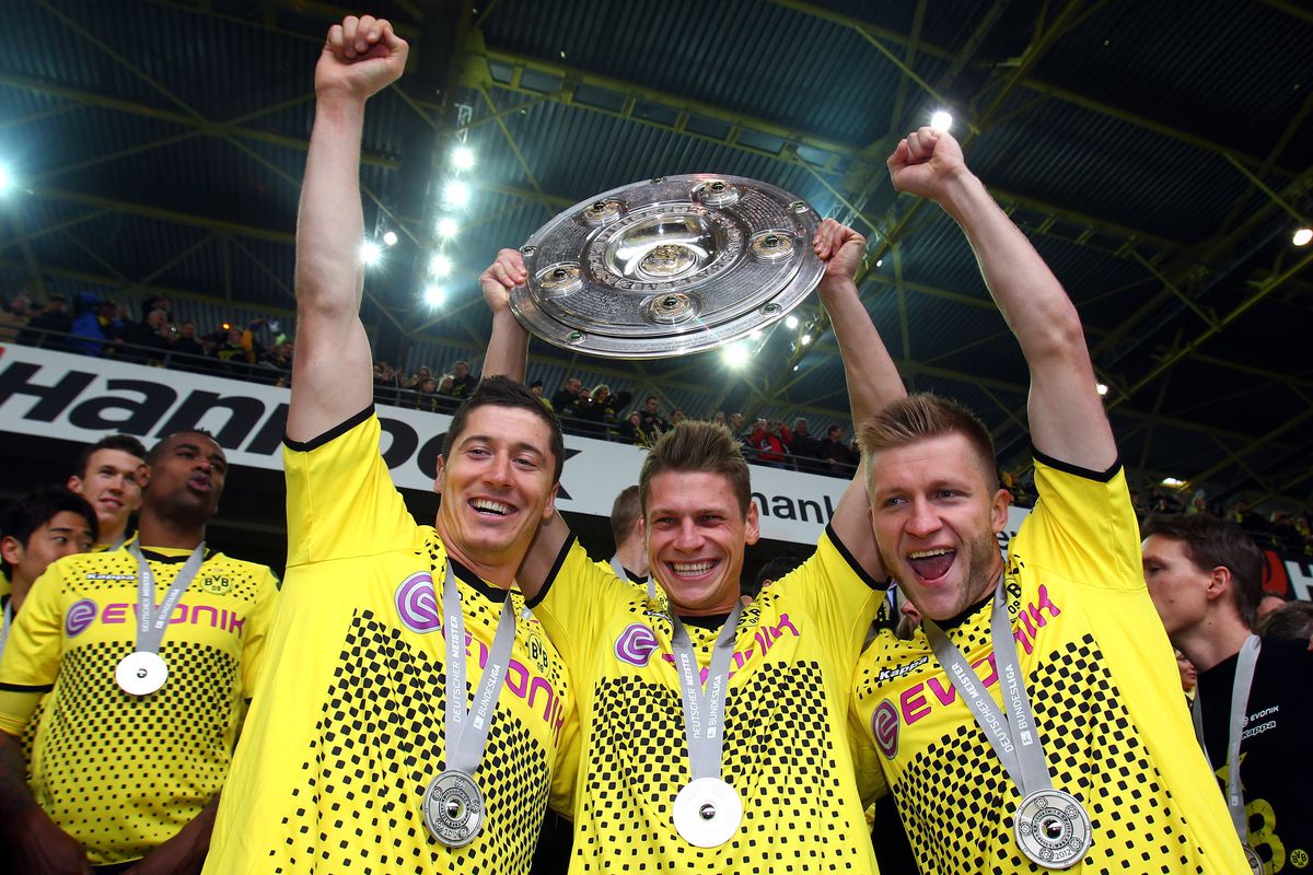 Robert Lewandowski, Lukas Piszczek, and Jakub Blaszczykowski celebrate while lifting the 2011-12 Bundesliga trophy
