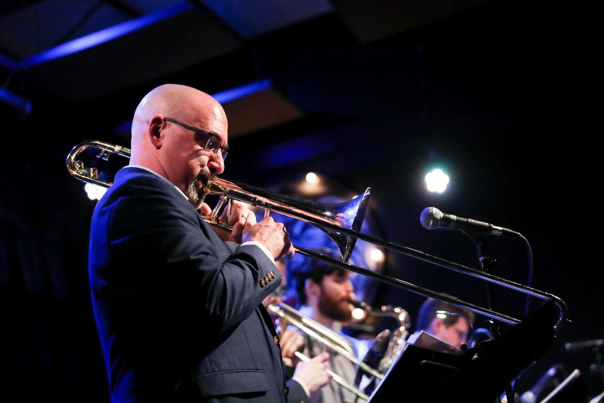 A bald man in sunglasses playing a trombone.