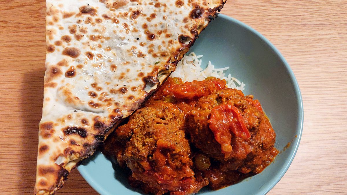 Two plump meatballs in red sauce sit on a bed of white rice, with a thin, crispy triangle of flatbread on the side.