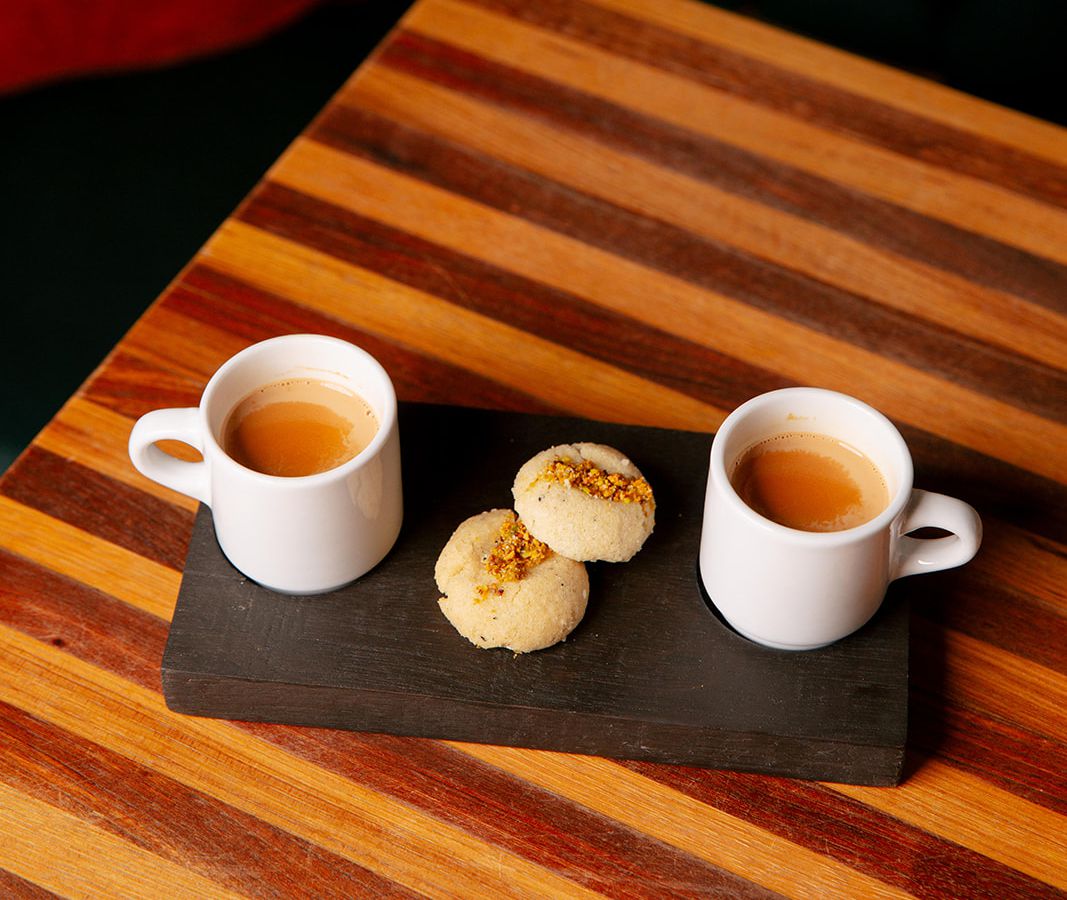 two cups of chai tea flanking two cookies on a black plate