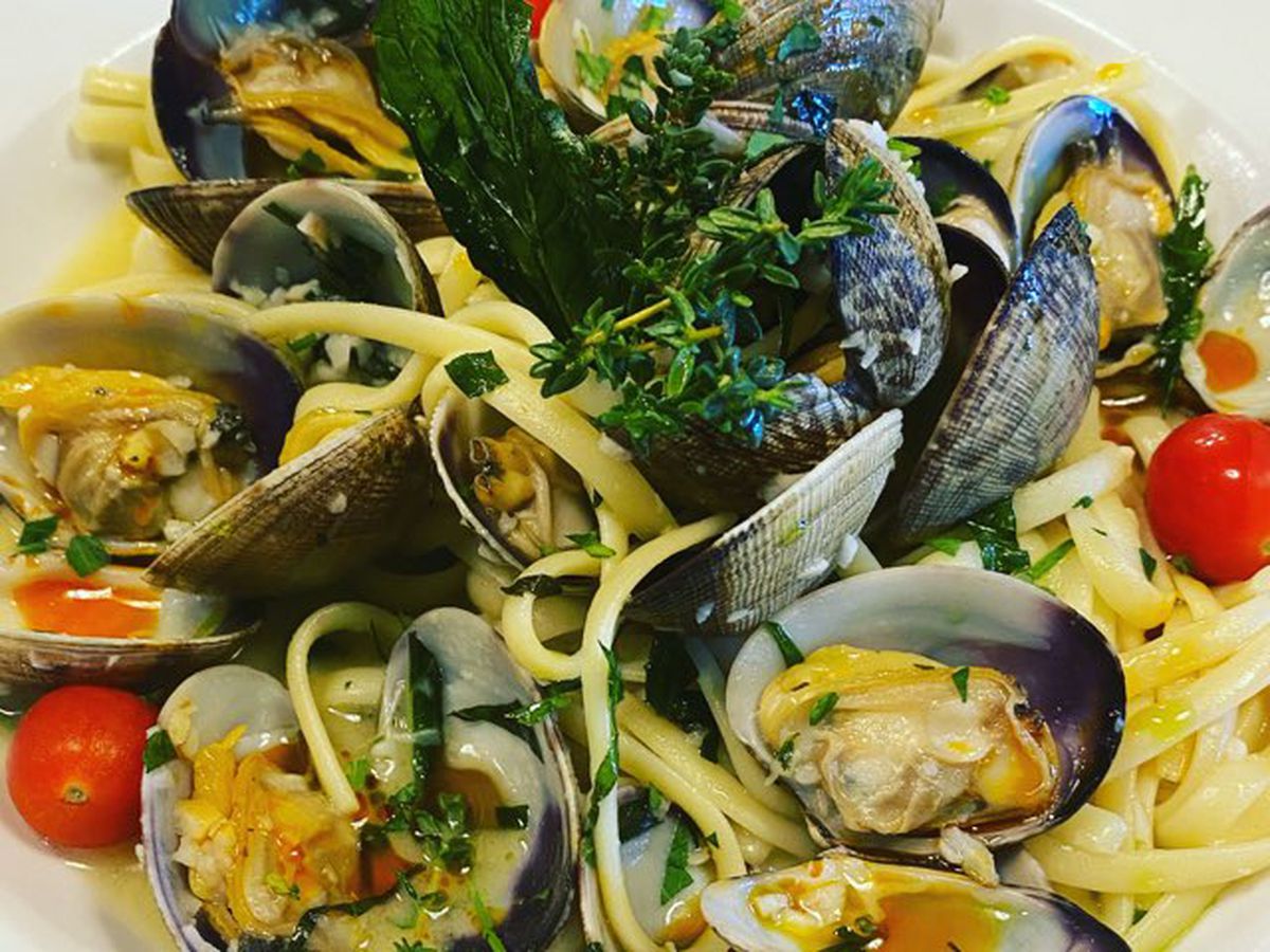 A plate of pasta and clams with cherry tomatoes and spices on a white plate.