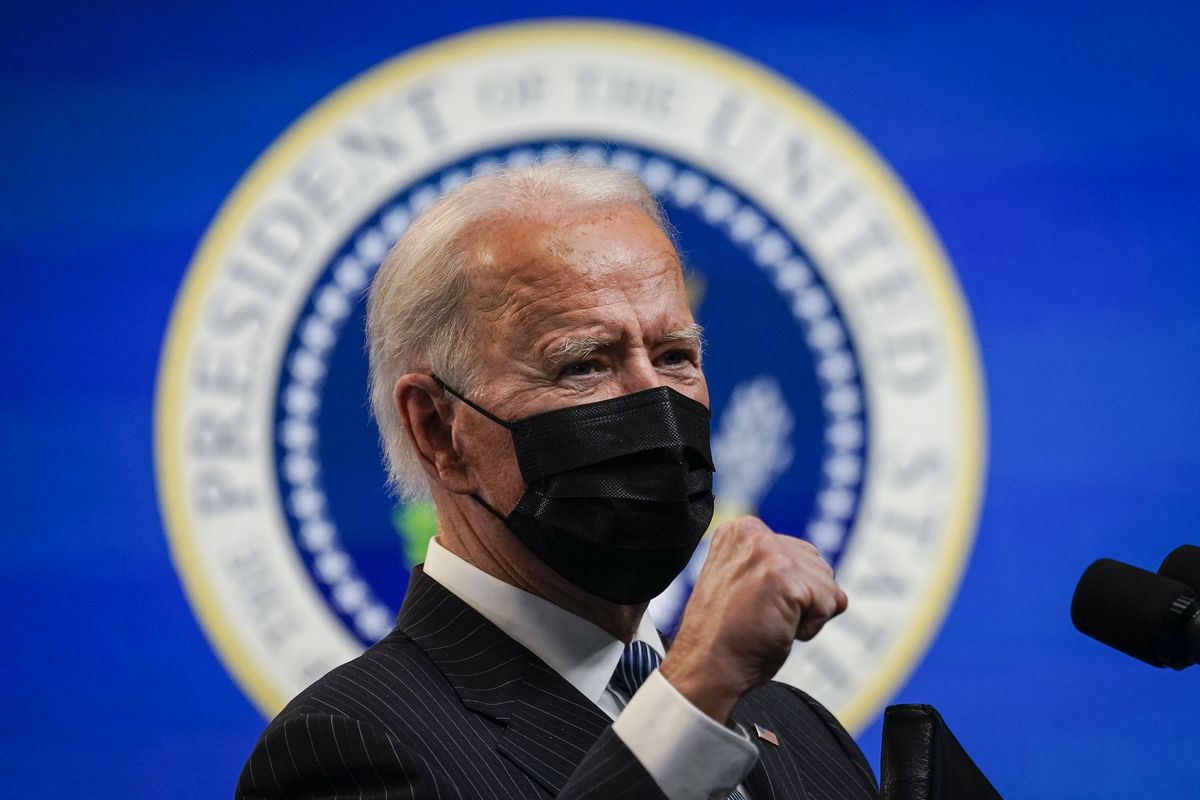 President Joe Biden wears a mask and holds a fist in front of him while speaking at a White House event.