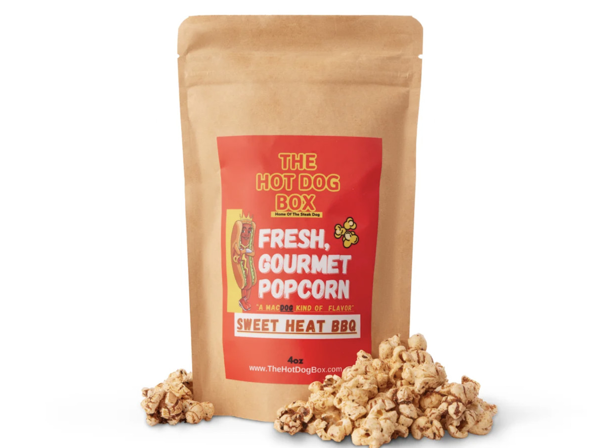 A brown paper bag of with a red label that reads “The Hot Dog Box Fresh, Gourmet Popcorn Sweet Heat BBQ.”