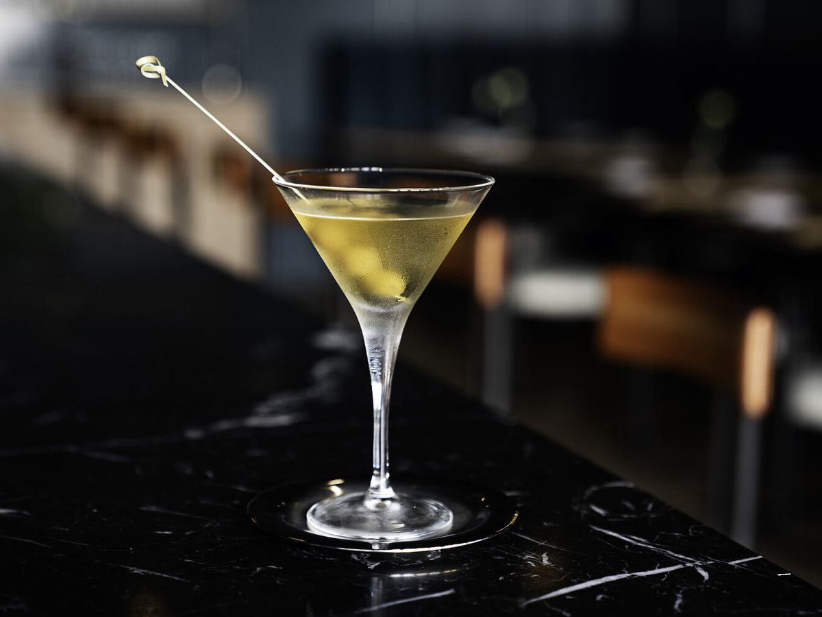 A yellow cocktail in a martini glass on a dark black bar.