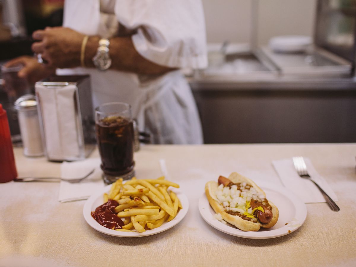 fries with ketchup on the side and a coney dog on a white diner counter with a man’s arm in the background
