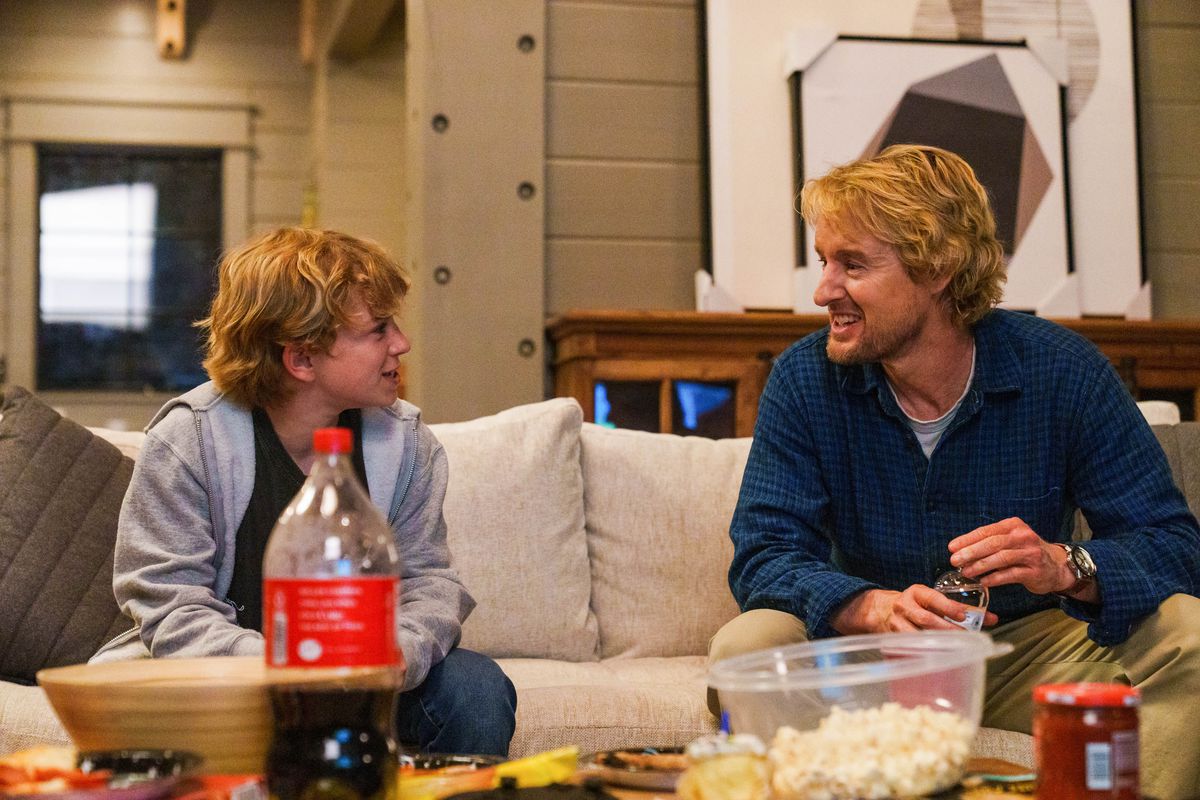 charlie, a young boy, sits with his dad, jack, on a couch with popcorn and soda in front of them