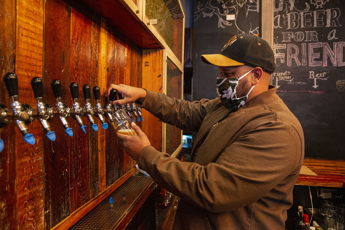 A man wearing a mask pours beer into a class out of a tap.
