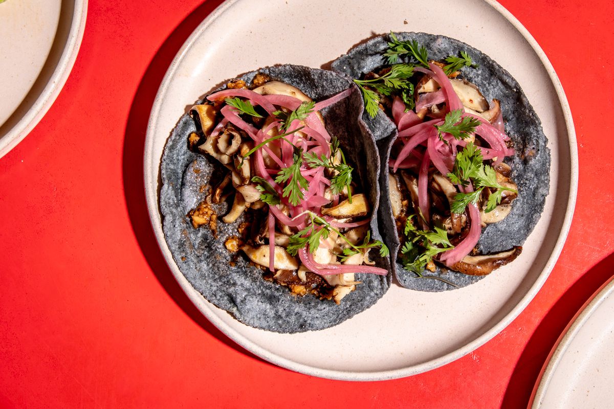 King oyster mushrooms, maitake mushroom paste, and pickled red onions sit atop blue corn tortillas as part of the mushroom taco preparation