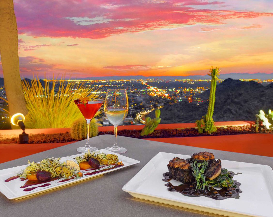 Two plates of food on a table overlooking am orange and pink-hued sky and a landscape dotted with cacti.