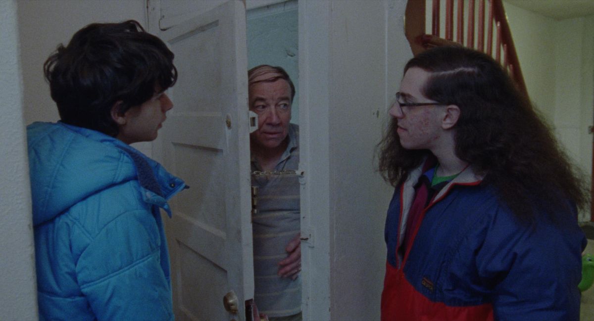 Robert and a friend stand in a doorway where a third man peers cautiously into Funny Pages