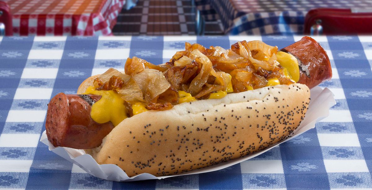 A kielbasa is nestled in a sesame-seed hot dog bun with grilled onions and yellow mustard.