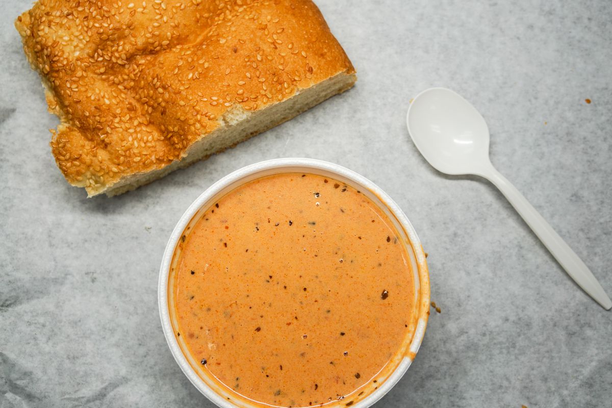A bowl of soup along with a square piece of bread.