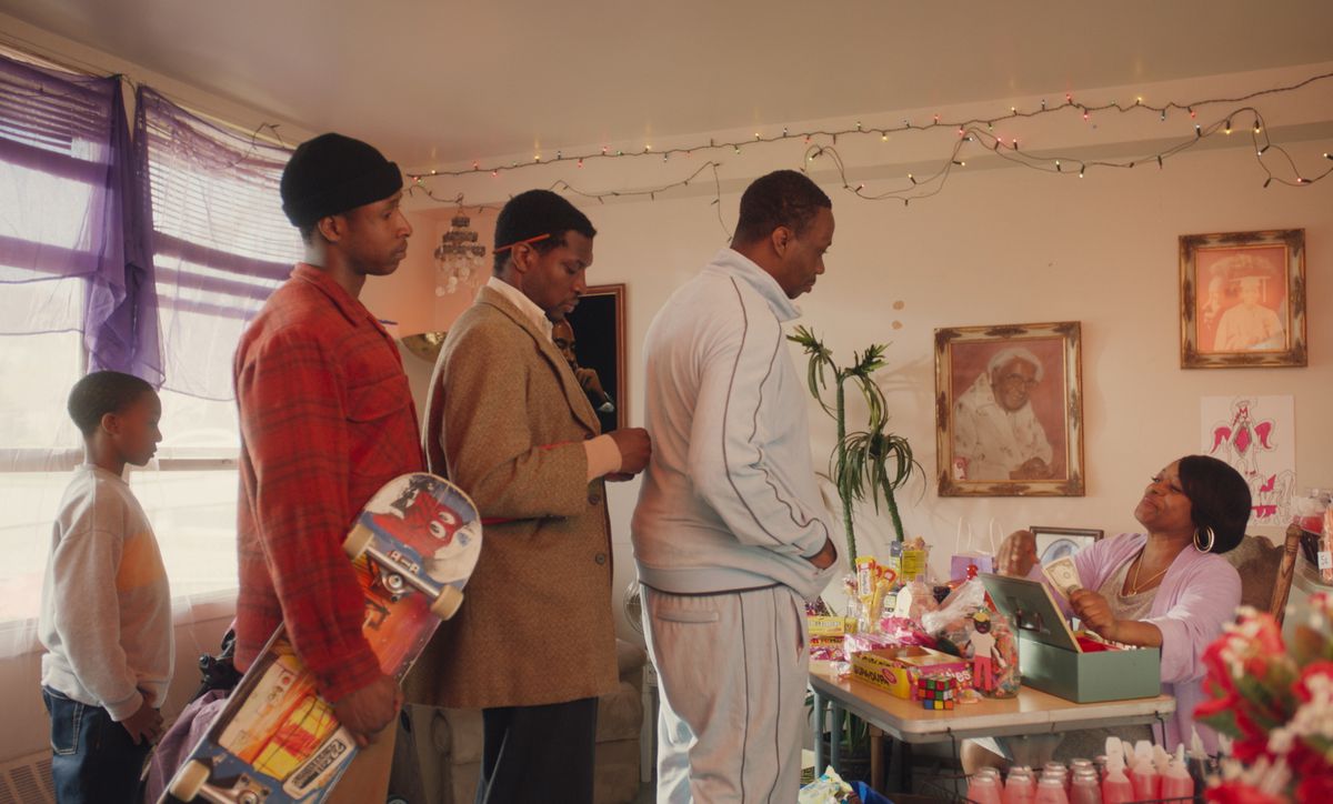 Three men and one boy line up inside the makeshift “candy house” to buy foods and goods from a lady at a table next to a cash register. It’s noon and there are white holiday lights strung up around the room’s ceiling. 