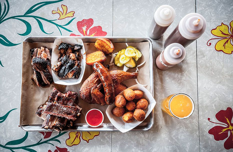 Overhead view of a platter of barbecue items with a side of sauces on a floral table