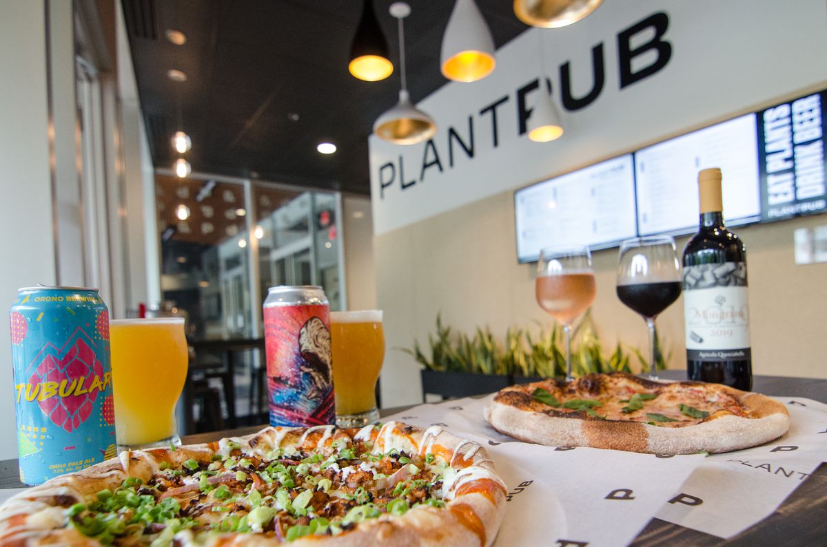 A table of pizza, beer, and wine is visible inside a casual restaurant, with PlantPub written on the wall.