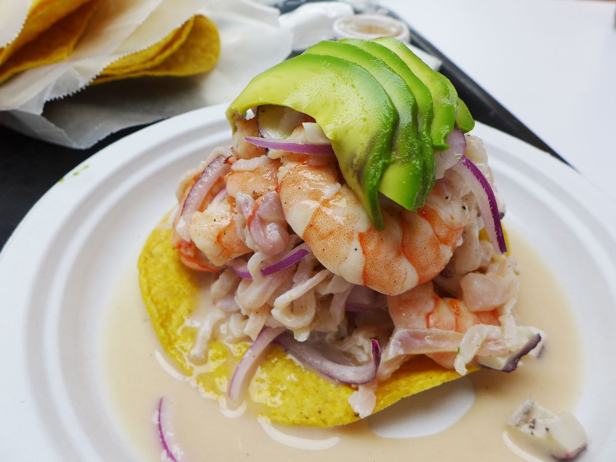 A round cracker with shrimp and other seafood piled high, topped with sliced and fanned avocado.