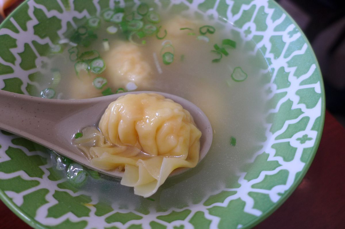 A spoon holds a dumpling above a green bowl.