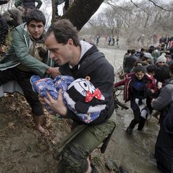 A man carries a baby as migrants cross a river, north of Idomeni, Greece, attempting to reach Macedonia on a route that would bypass the border fence, Monday, March 14, 2016. Hundreds of migrants and refugees walked out of an overcrowded camp on the Greek-Macedonian border Monday, determined to use a dangerous crossing to head north.