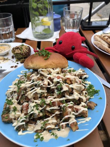 A huge plate of chicken topped with chopped vegetables and garlic sauce, with a bun near the far end, arranged beside a plush toy lobster