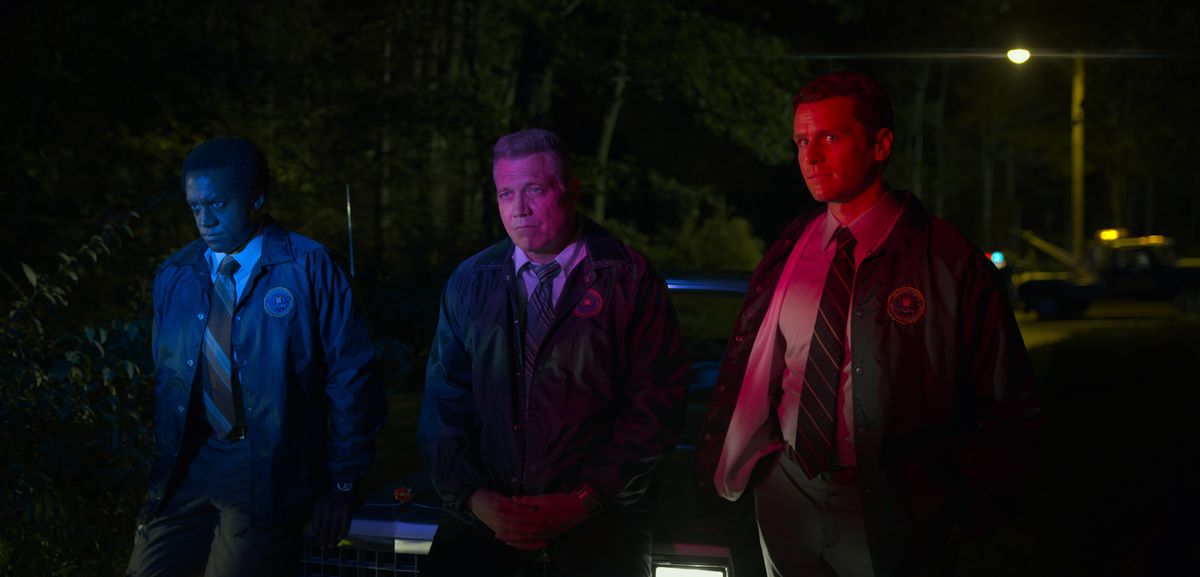 Albert Jones, Holt McCallany, Jonathan Groff leaning against the hood of a car while lit by the police sirens in episode five of Mindhunter season 2.