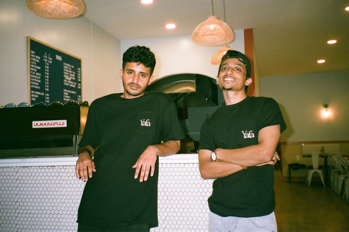Cousins Ali Suliman and Hakim Sulaimani, both wearing black t-shirts, stand next to each other in their cafe.
