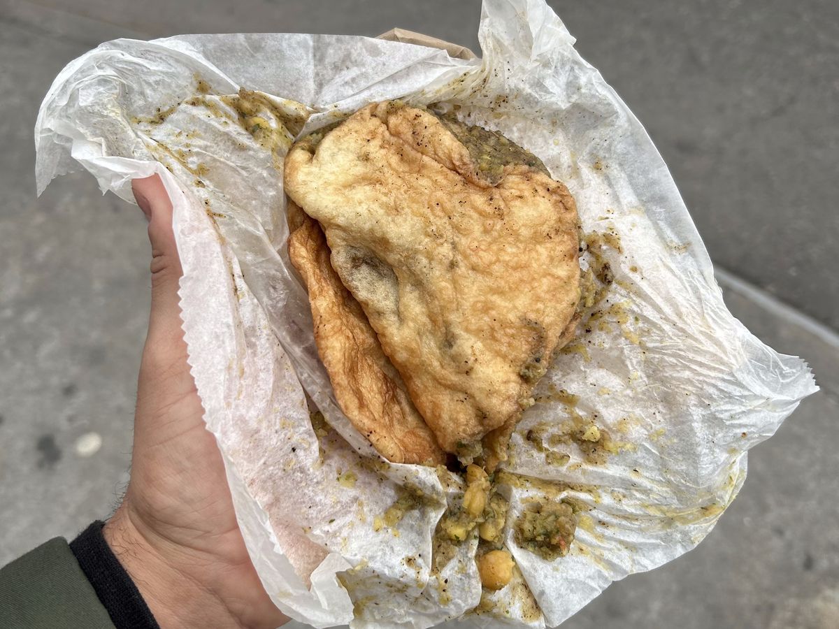 A hand holds an unwrapped Trinidadian double from A&amp;A Bake Doubles and Roti in Bed-Stuy, Brooklyn.