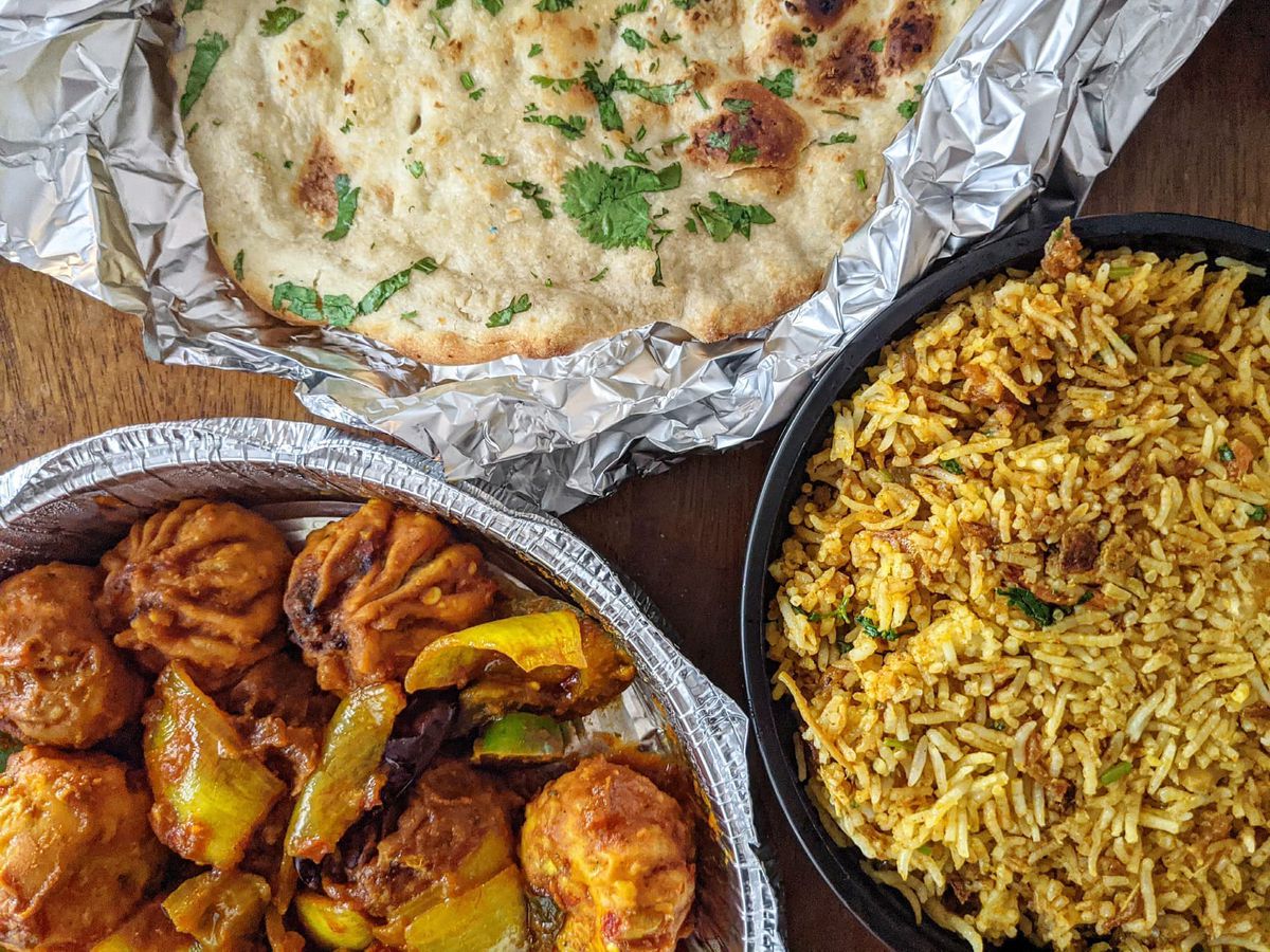 Takeout containers hold fried Nepali dumplings with sauteed peppers and onions, a yellowish rice and chicken dish, and naan.