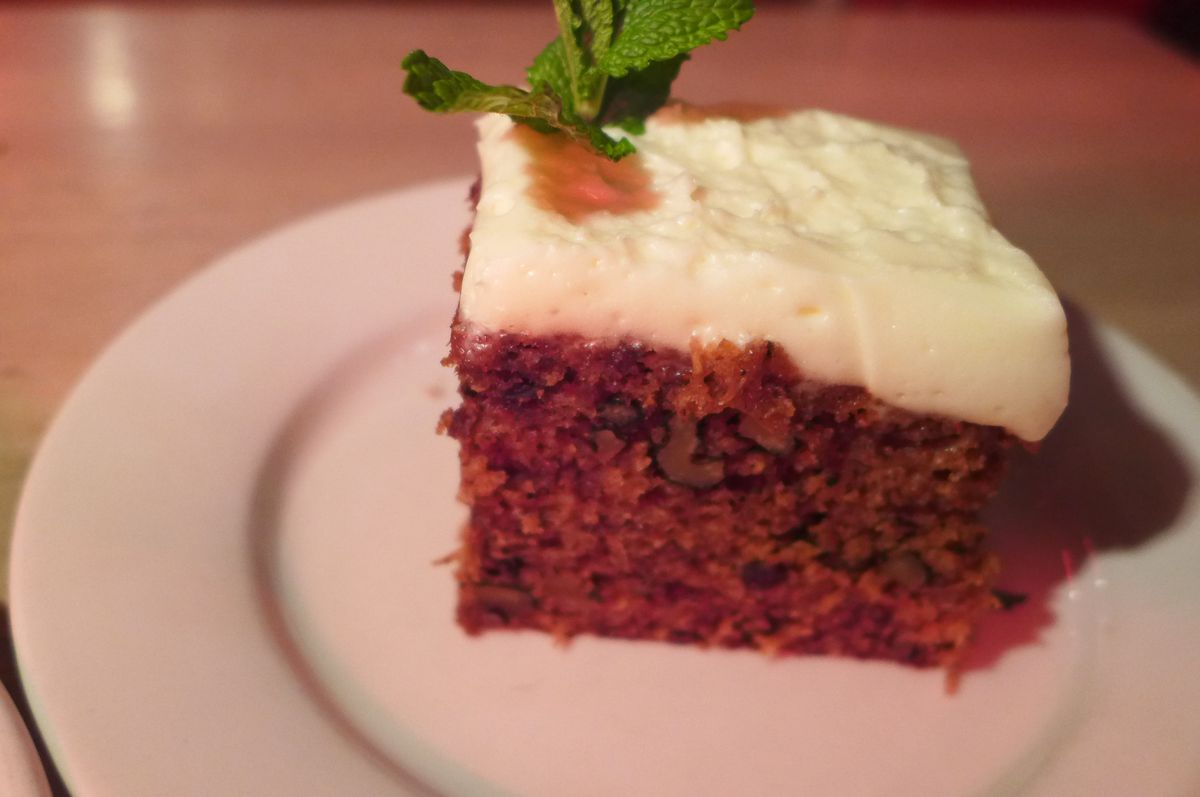 A square of cake with white frosting and a sprig of mint sticking out the top.