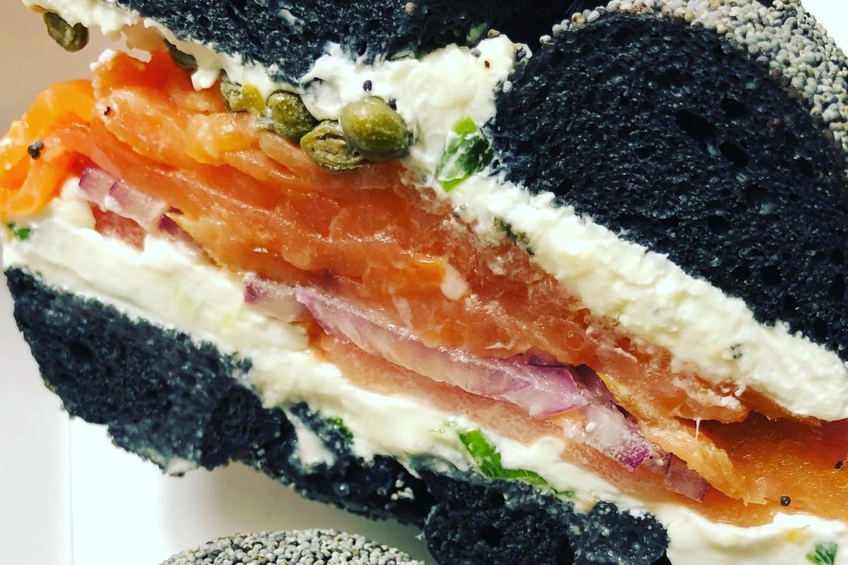 A bagel half with lox, capers, tomato, and onion, with jet-black bagel dough with sesame seeds.