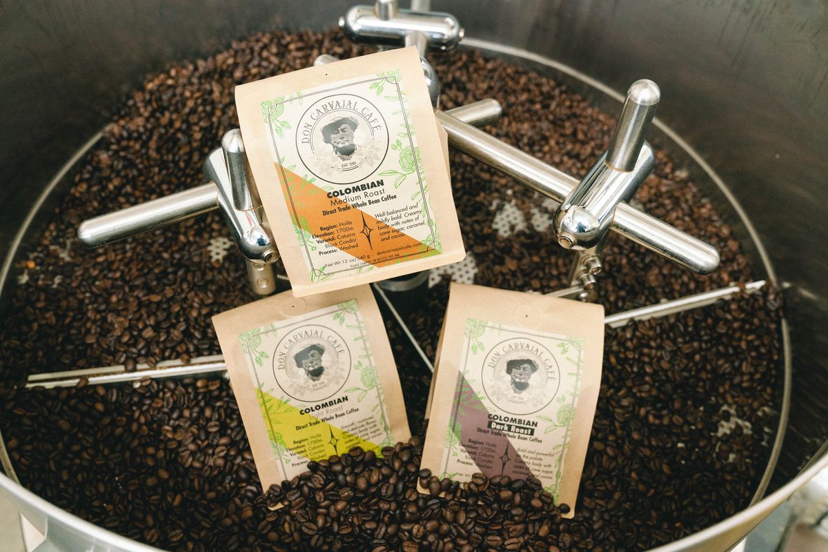 Three bags of coffee beans propped up among loose coffee beans in a roaster.