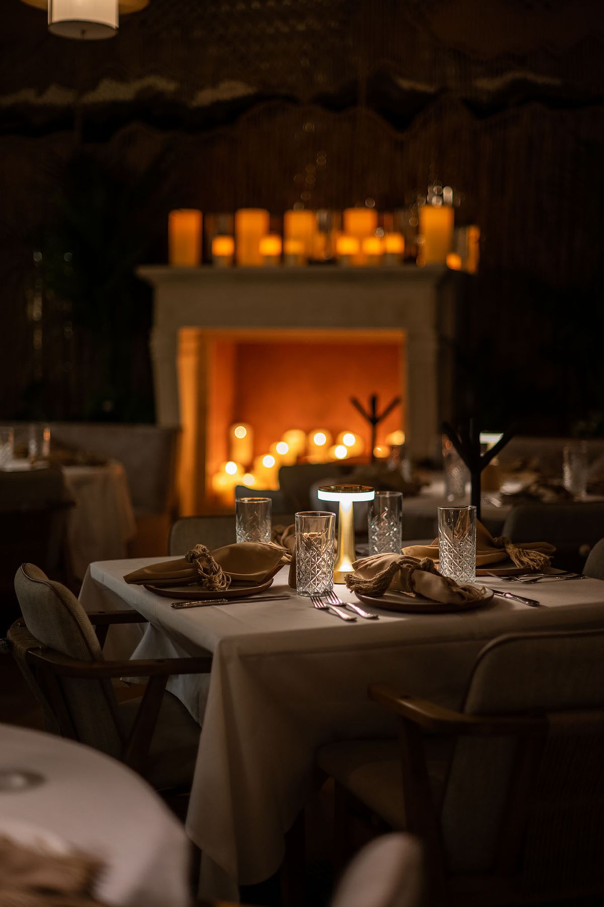 A fireplace filled with tall white candles inside of a dinner restaurant.