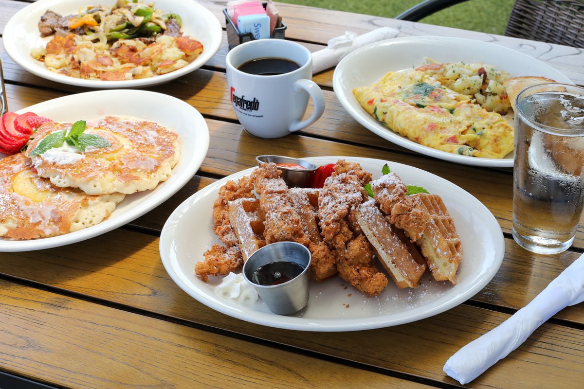 A brunch spread of pancakes, chicken and waffles, and omelettes are laid out on a wooden tabletop.
