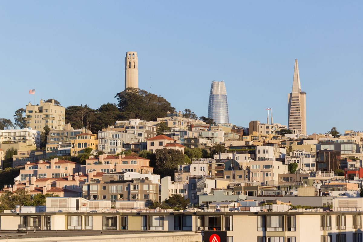 Coit Tower, Salesforce Tower, and the Transamerica Pyramid all peeking over the top of a hill.