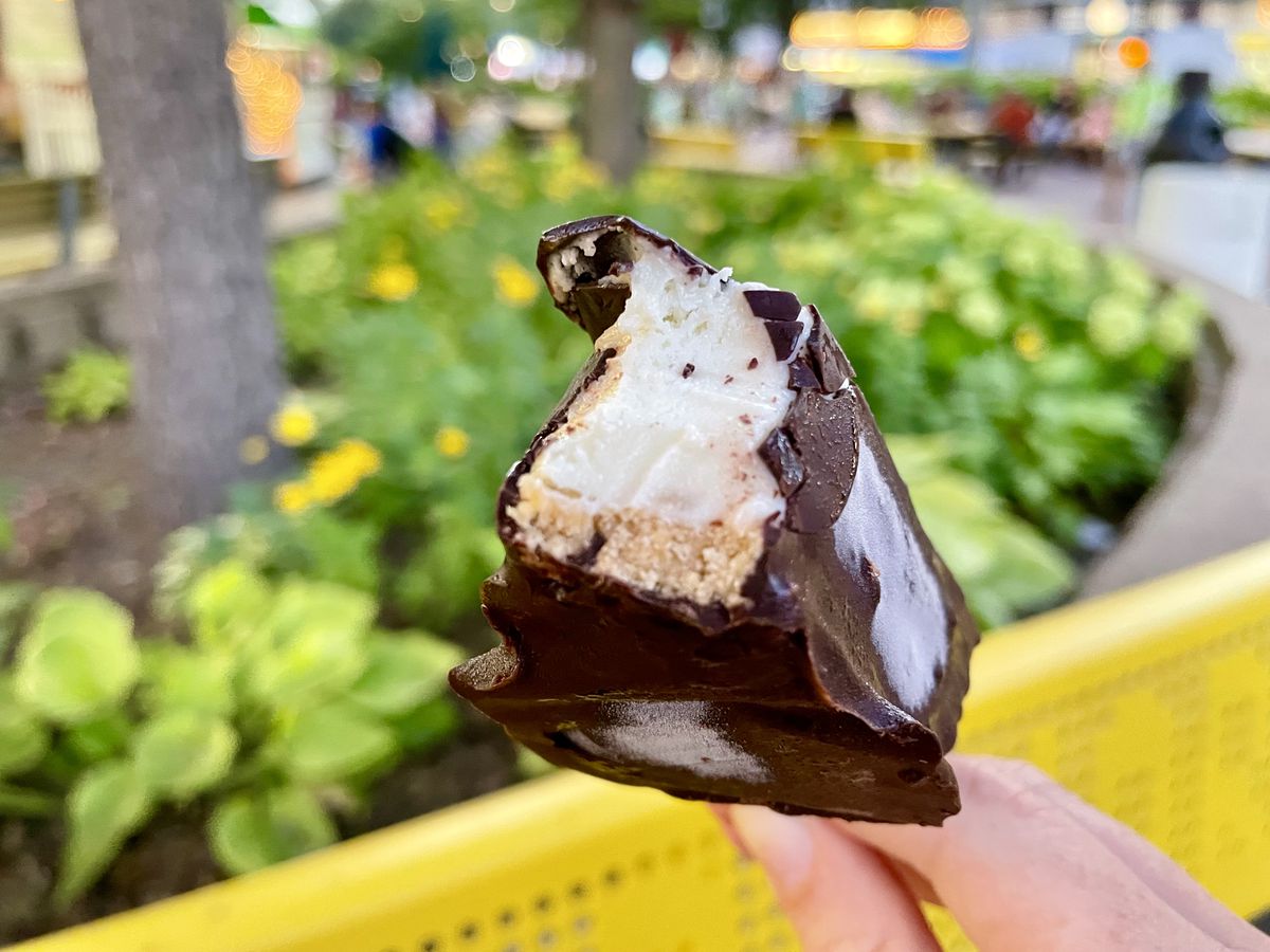 A hand holding a piece of chocolate-covered key lime pie with a bite out of it.