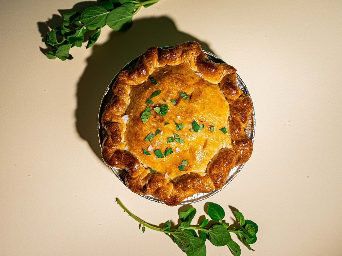 A golden pot pie garnished with herbs on a beige background. 