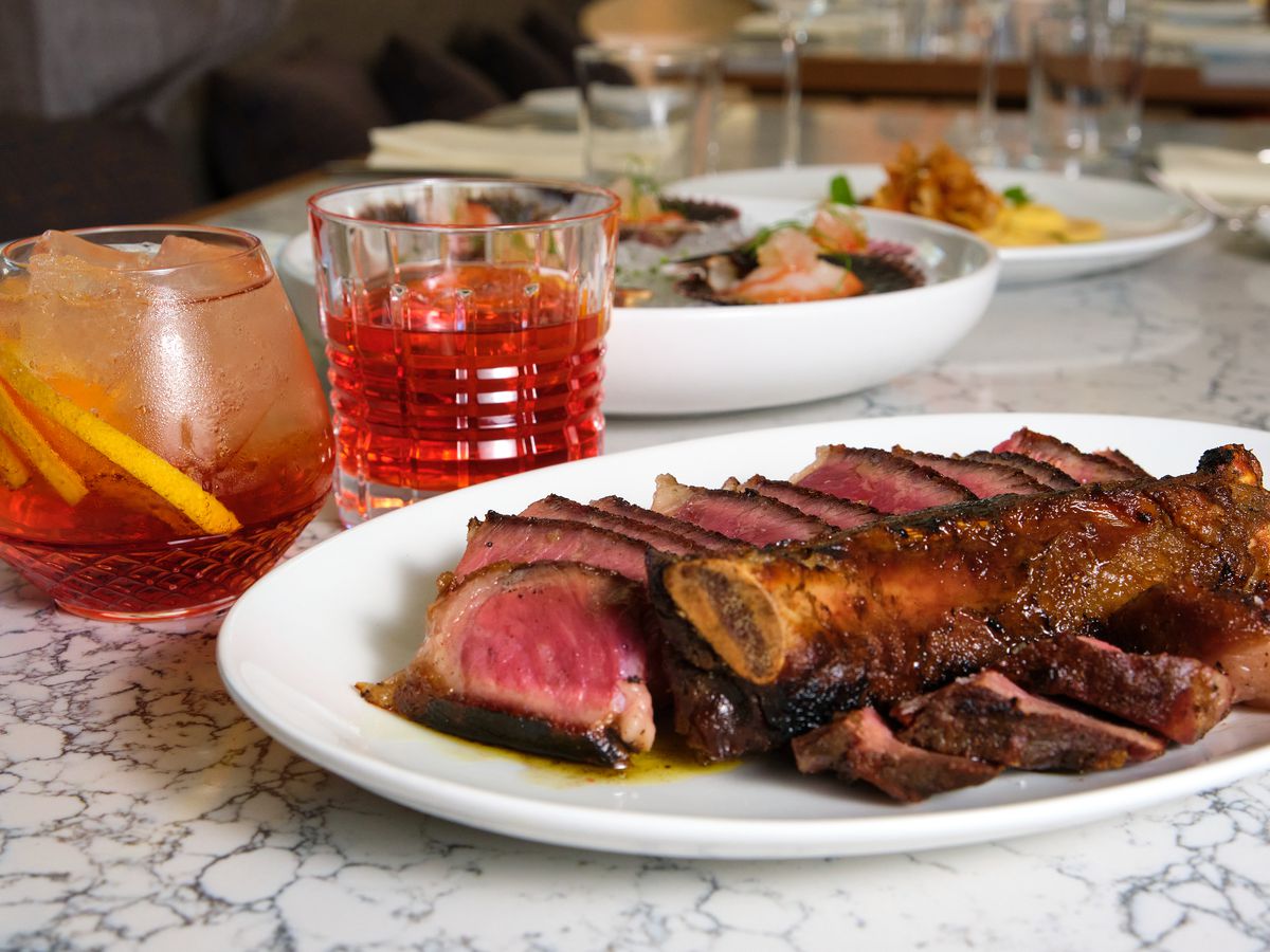 A steak on a white plate and two cocktails