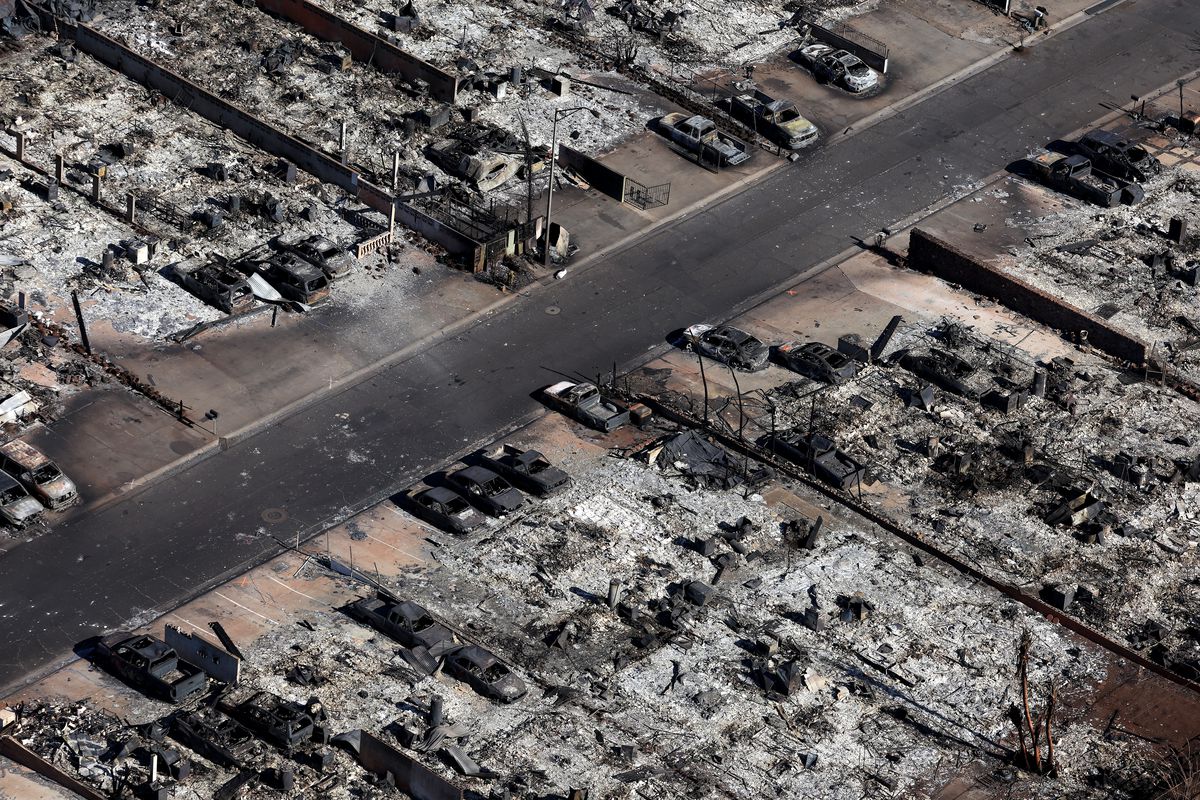 A former grid of streets in a small town, seen from above, is now outlined in shades of ash and char, every building, car and tree now burnt, gray-coated debris.