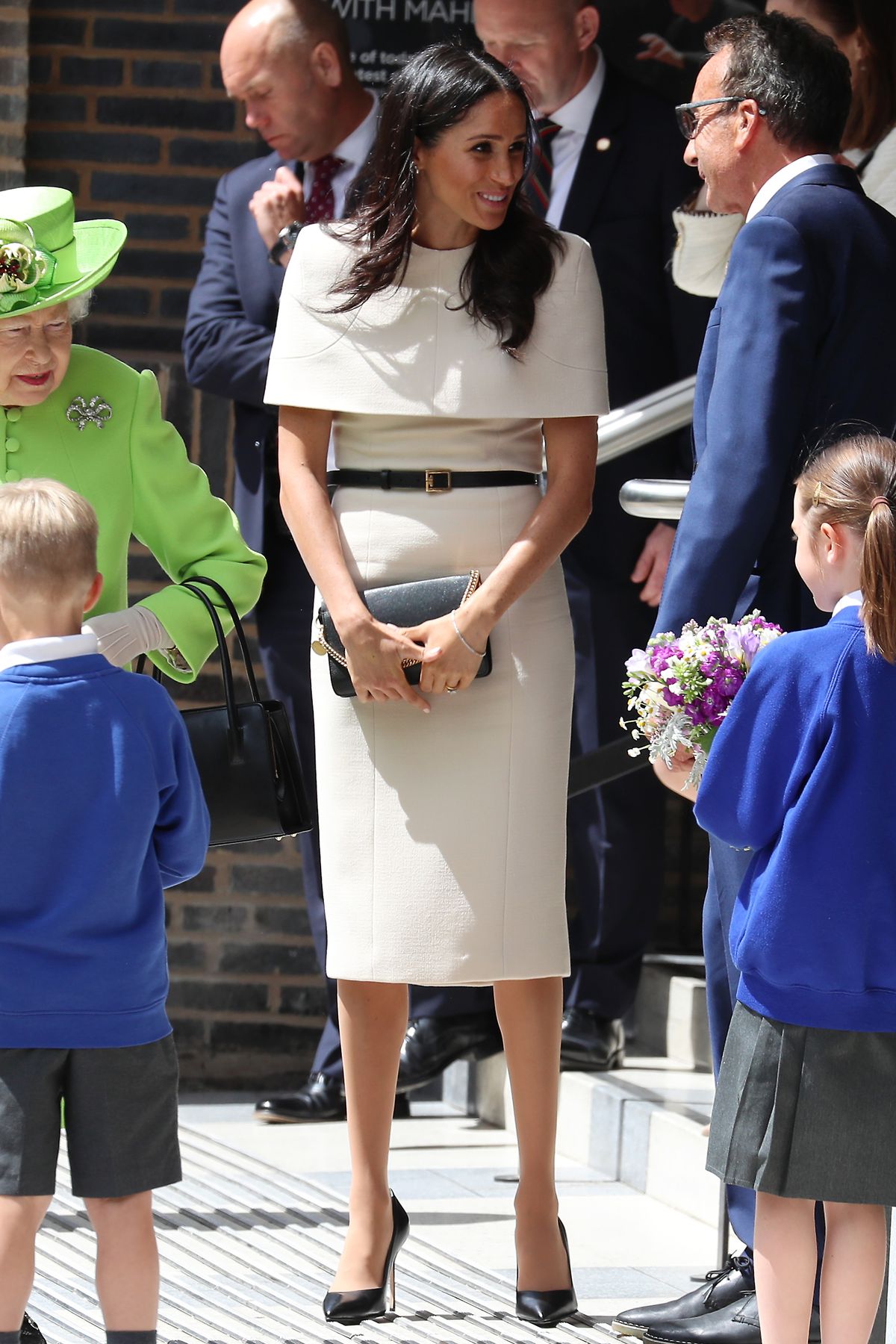 Markle greets people while standing next to the queen.