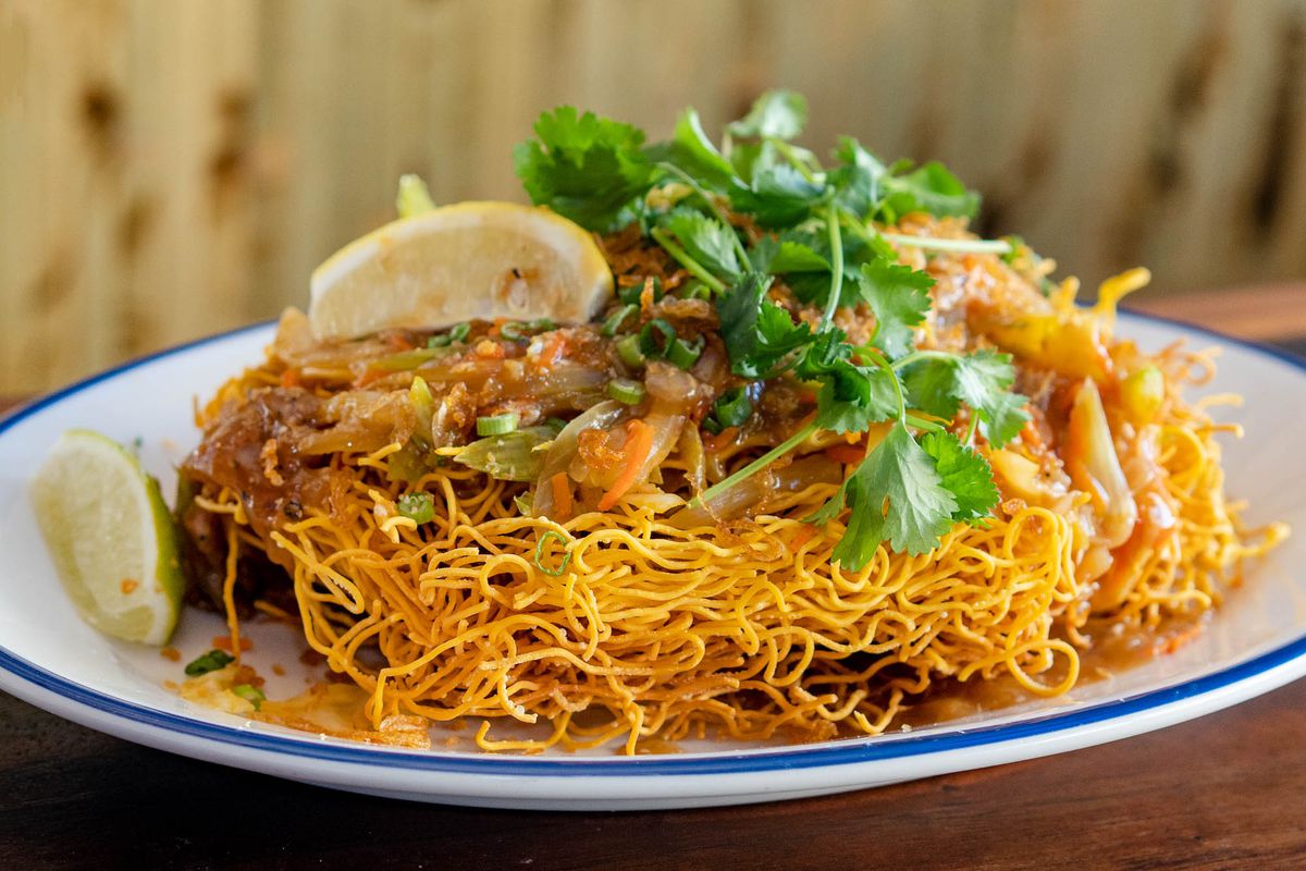 A nest of crispy egg-colored noodles with some lemon wedges and cilantro on top.