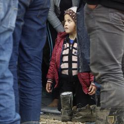 A Syrian refugee girl kneels on a tent, as men stand in front, in an improvised camp on the border line between Macedonia and Serbia near the northern Macedonian village of Tabanovce, Friday, March 11, 2016. About 1,500 refugees remain stranded at the Macedonian border with Serbia as the borders on the Balkan migrant route are closing. 