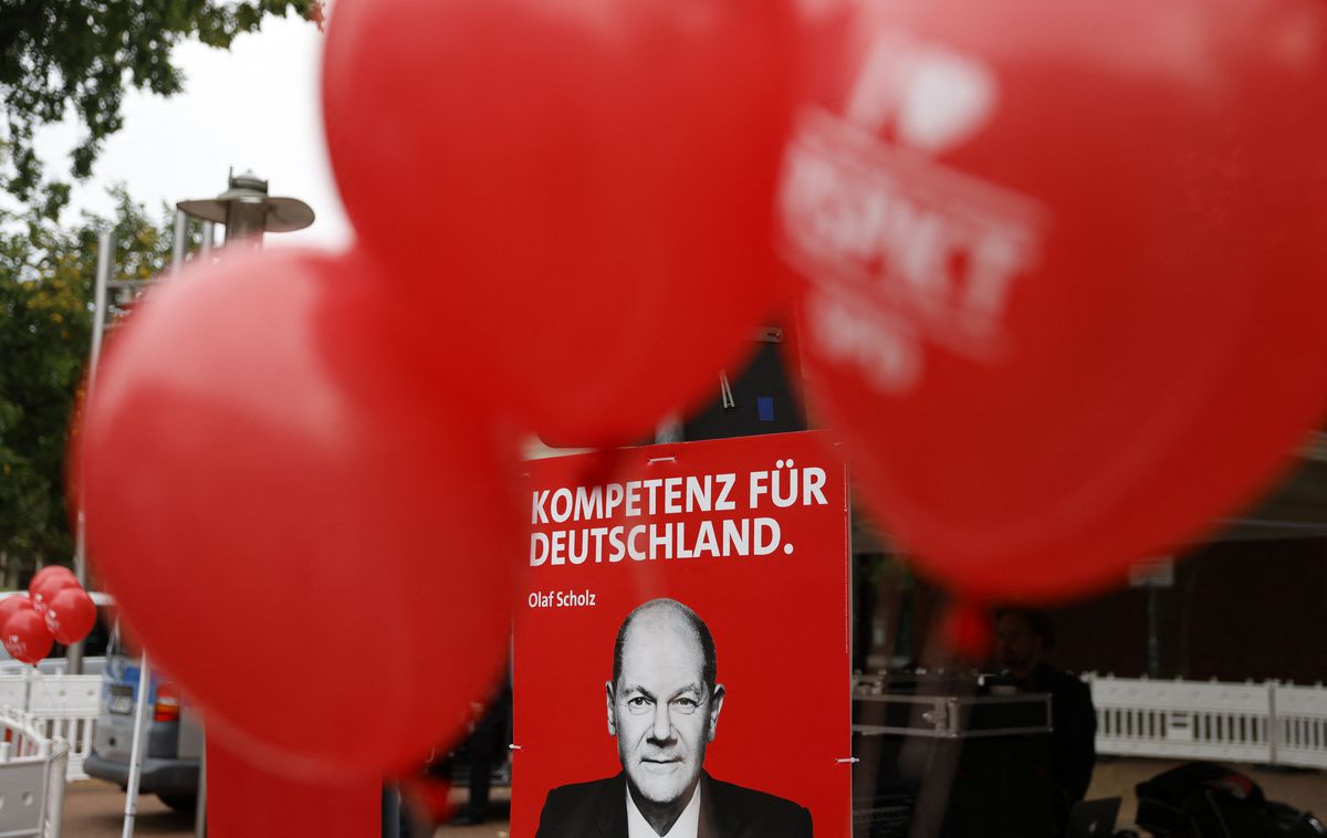 Large red balloons surround a political poster with Olaf Scholz’s face and the slogan, “Kompetenz fur Deutschland.”