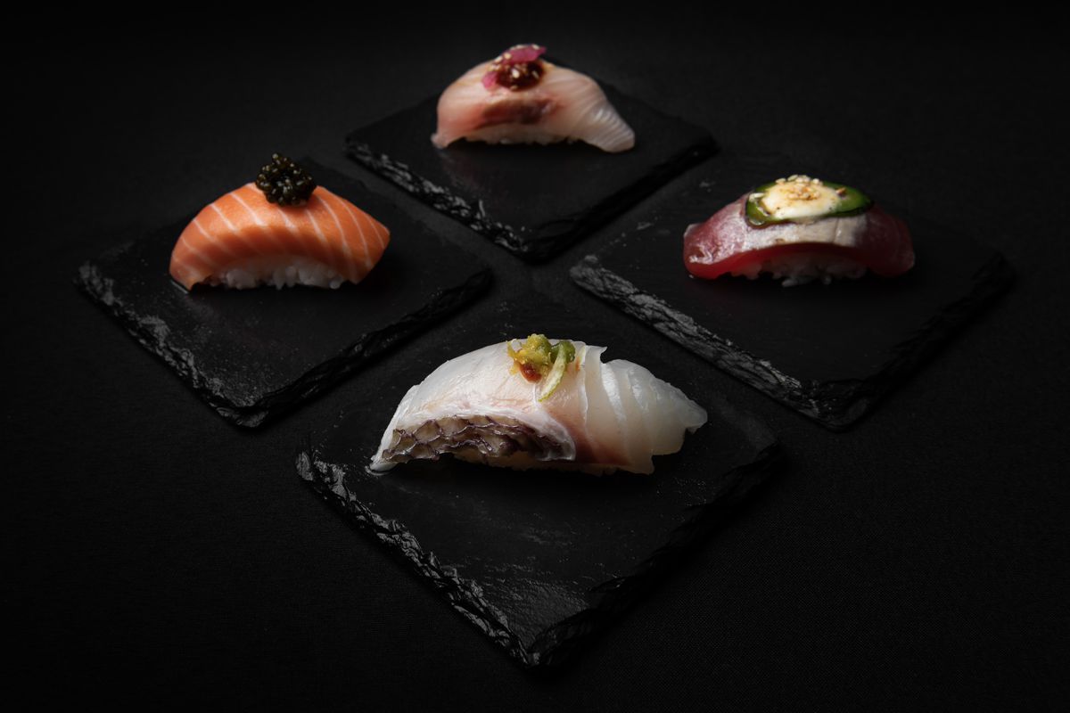 Four pieces of sushi on slate plates on a dark table.