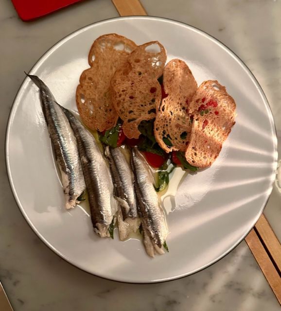four white anchovies with toasts and a salad. 