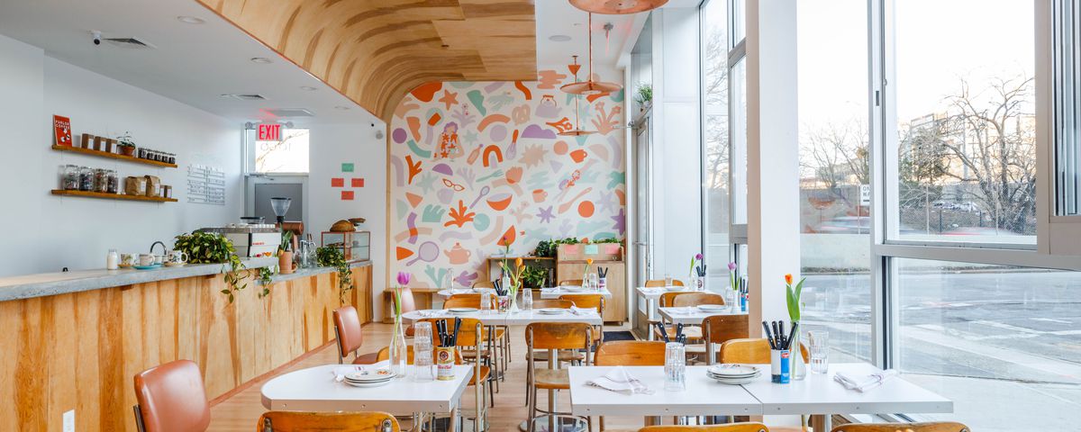 The interior at Gertie has windows on the left and a pastel-colored geometric mural on the back