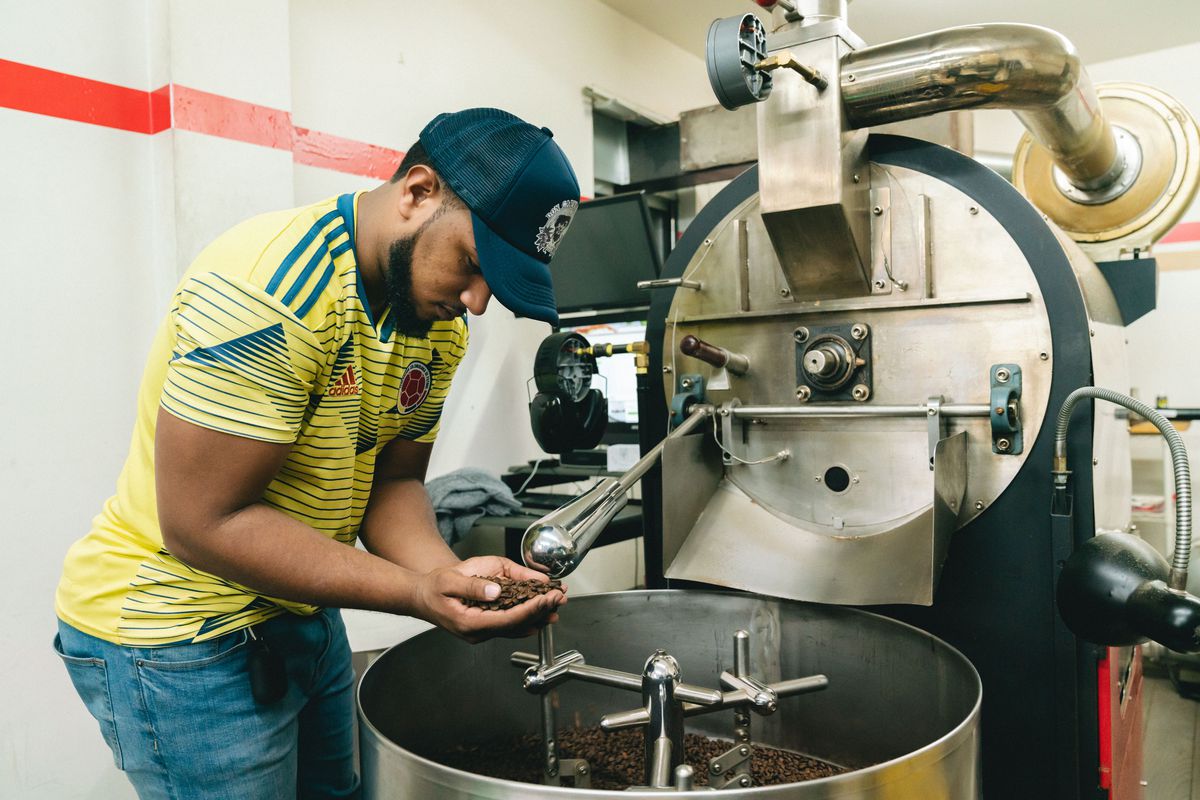 Hector Carvajal leans over a coffee roaster inside a factory warehouse, inspecting the beans.
