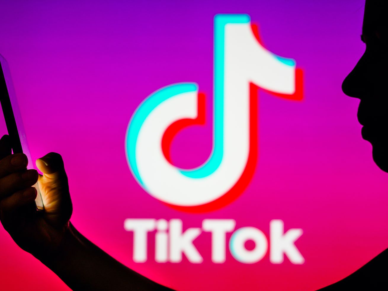 In this photo illustration, a woman’s silhouette holds a smartphone with the TikTok logo in the background.